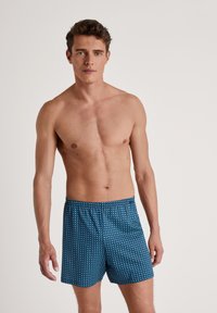 Blauwe boxershort met een stippenpatroon, voorzien van een elastische tailleband en ademend materiaal, gedragen door een model zonder shirt.