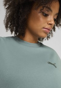 Lys grøn kortærmet T-shirt med ribbet halsudskæring og et lille broderet logo på venstre bryst. Blød, glat tekstur.