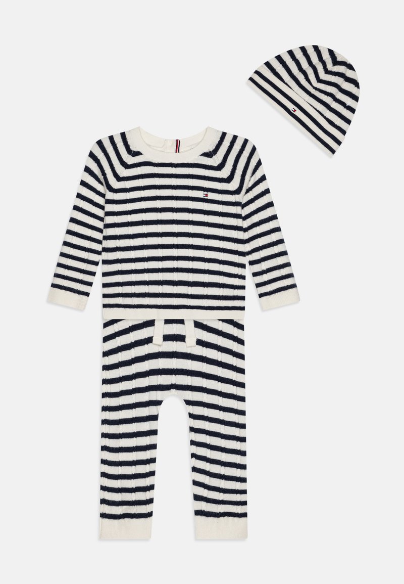 Pleteni dvodelni komplet v kremni barvi z mornarsko modrimi horizontalnimi črtami. Opremljen je z dolgimi rokavi, okroglo ovratnico in usklajeno črtasto kapico.