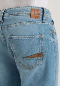 I jeans in denim azzurro chiaro presentano una patch in pelle con logo, due tasche posteriori con cuciture in vista e un design unico delle tasche angolate.