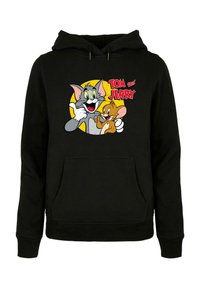 Sweat à capuche noir avec un motif graphique devant représentant les personnages de dessin animé Tom et Jerry, avec des couleurs vives et un fond rond jaune.