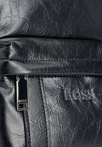 Czarna torebka z teksturowanej skóry, z zamknięciem na zamek i srebrnym akcentem w postaci logo "BOSS". Wysokiej jakości wykończenie z marszczonym wzorem.