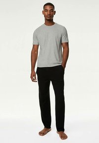 Graues Kurzarm-T-Shirt kombiniert mit schwarzer Hose, mit lockerer Passform und weichem Stoff, präsentiert an einem stehenden männlichen Model.