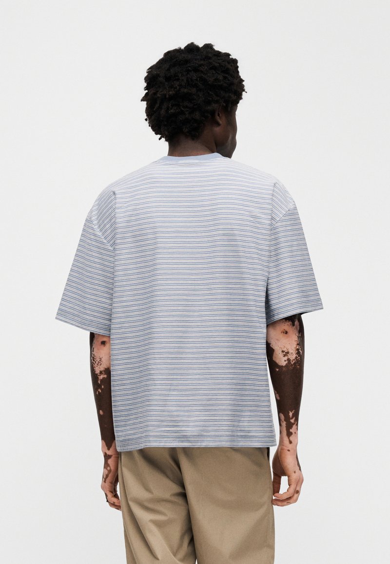 Striped short-sleeve shirt in light blue and white, featuring a round neckline and loose fit, made from soft fabric, with a simple design.