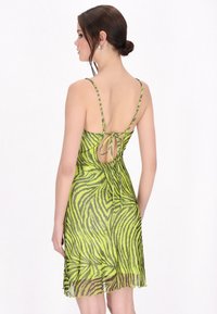 Rochie cu imprimeu zebră verde, cu bretele subțiri, spate deschis legat în talie și o ușoară evazare la tiv, realizată dintr-un material translucid.
