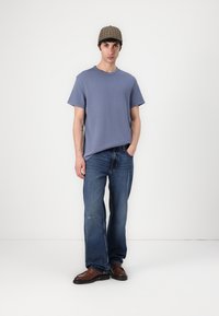 Blå bomulls t-skjorte med kort erme, kombinert med løse mørke denim jeans. Brune skinnsko og en rutete caps fullfører antrekket.