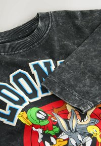 Black acid-wash long sleeve shirt with colorful Looney Tunes characters and bold white-blue letters "LOONEY" on the front.