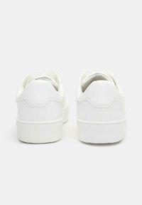 Sneakers bianchi con una superficie in pelle liscia, parte posteriore rotonda e cuciture tono su tono. Suola in gomma bianca spessa e semplice design con lacci.