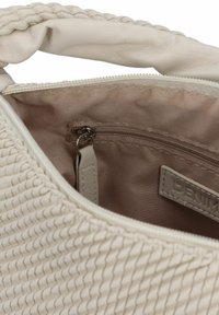 Intérieur d'un sac à main en beige tissé montrant une poche zippée, une doublure lisse et une étiquette. Le sac a un extérieur doux et texturé avec une anse tressée.
