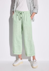 Ljusgröna linnebyxor med vida ben och dragsko i midjan, med en avslappnad passform och uppvikta nederkanter, som bärs med vita sneakers.