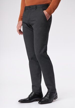 Charcoalgrijze, taps toelopende broek van textuurstof, met riemlussen, zijzakken en een sluiting met knoop aan de voorkant, gecombineerd met zwarte schoenen.