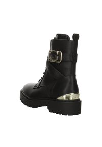 Bottine en cuir texturé noir avec semelle épaisse, bride à boucle dorée sur le côté et accent doré sur le talon embossé avec la marque "GUESS".