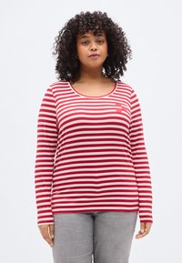 Κόκκινο και λευκό ριγέ μακρυμάνικο πουκάμισο με στρογγυλή λαιμόκοψη, που διαθέτει μια μικρή λεπτομέρεια καρδιάς στο αριστερό στήθος και μαλακή υφή.