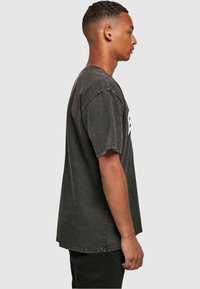 Camiseta de algodón gris con mangas cortas, corte relajado, costuras laterales y letras gráficas en blanco legibles en el pecho. Textura suave y desgastada.