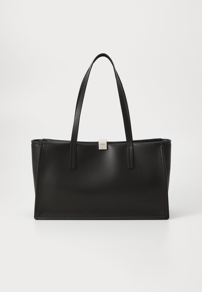 Sac cabas rectangulaire en cuir noir avec deux fines anses et une petite boucle argentée sur fond blanc.