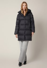 Czarna puchowa kurtka z kapturem, z pikowanym wzorem, z zamkiem błyskawicznym z przodu i bocznymi kieszeniami. Połączona z jasnoszarymi spodniami o szerokich nogawkach.