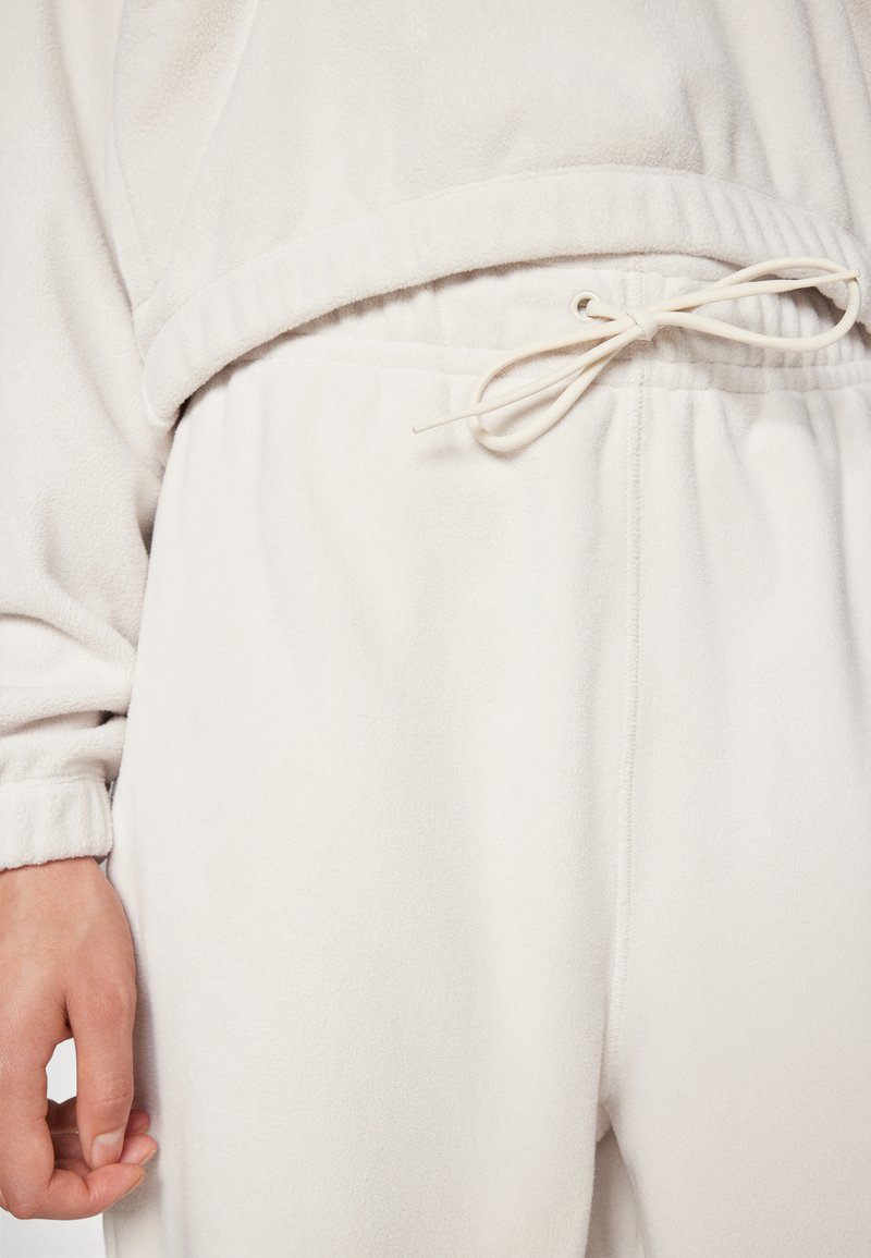 Jasno beżowy zestaw odzieży domowej z polarowego materiału, z wiązanym w pasie i elastycznymi mankietami, który cechuje miękka tekstura i luźny krój.