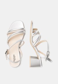 Sandales à talons hauts argentées avec plusieurs brides entrecroisées, finition métallisée et accents décoratifs. Comprend une fermeture à boucle et un talon carré.