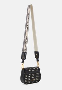 Bolso bandolera negro texturizado con patrón trenzado, herrajes dorados y correa blanca ajustable impresa con "KARL LAGERFELD" en negro.