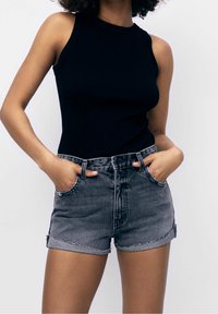 Haut sans manches noir côtelé associé à un short en denim gris taille haute avec un ourlet effiloché et des poches avant.