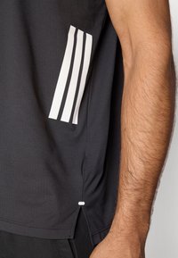 Camiseta deportiva negra con tres rayas blancas en el lado izquierdo, textura suave y un pequeño detalle blanco en el dobladillo.
