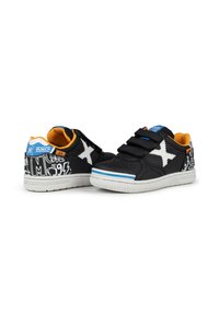 Zapatillas negras con detalle de estrella blanca, correas de Velcro, interior naranja y parte superior negra texturizada con un estampado gráfico en el talón.