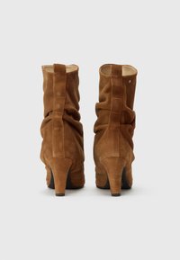 Bruine suède enkellaarsjes met hak, voorzien van een gerimpelde textuur, een achteruittrekbare lus en een gladde binnenvoering. Ontworpen met een stilettohak voor extra lengte.