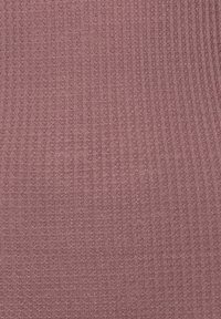 Strickstoff in zartem Rosaton mit einem strukturierten Muster aus kleinen erhöhten Punkten. Das Material scheint dehnbar und leicht zu sein.