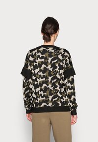 Suéter con patrón de camuflaje en negro y verde oliva, de tejido texturizado, con detalles de volantes en las mangas y puños acanalados.