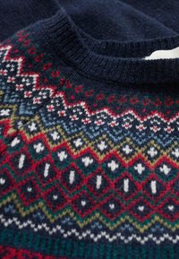 Pull en tricot avec une base bleu marine et des motifs géométriques multicolores complexes en rouge, vert, blanc et jaune. Finition texturée.