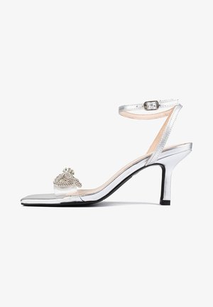 Stříbrné sandály na vysokém podpatku s průhledným páskem a dekorativními akcenty z rhinestones. Mají zaoblenou špičku a štíhlý pásek kolem kotníku.