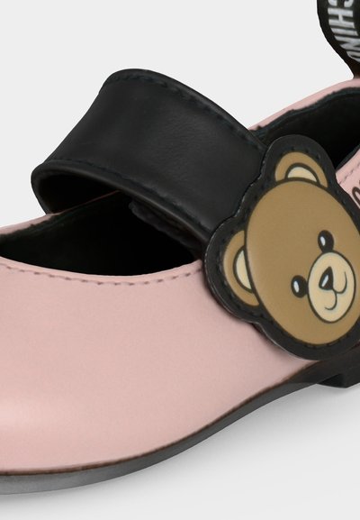Chaussure d'enfant rose avec une bride noire présentant un visage souriant d'ours en peluche marron sur le côté.