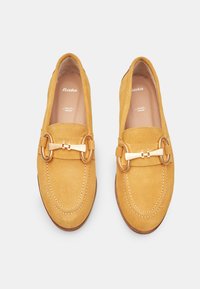 Misiņā dzeltenās zamšādas loafers ar zelta toņa metāla sprādzi, apaļu purngali un kontrastējošiem dūriem malās.