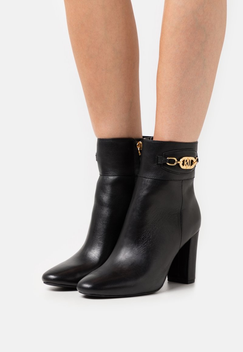 Black leather ankle boots with a pointed toe, block heel, and gold hardware detail on the cuff. Textured finish. Side zipper closure.