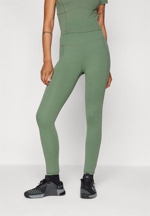 Tettsittende grønne leggings med en jevn tekstur, som har doble sidesømmer og høy midje. Kombinert med svarte treningssko.
