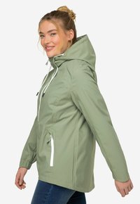 Světle zelená nepromokavá bunda s kapucí, elastickými manžetami a předními kapsami. Má bílé zipové detaily a volnější siluetu.
