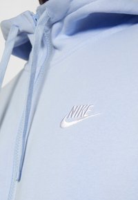 Ljusblå zip-up hoodie i mjukt tyg, med en justerbar huva och en vit broderad Nike-logotyp på bröstet.