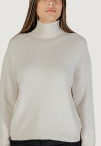 Pull à col roulé blanc en tricot doux avec des accents de paillettes subtiles, présentant une coupe décontractée et des poignets et un ourlet en côtes.