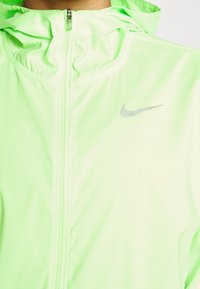 Gros plan d’une veste zippée vert néon avec capuche et logo Nike réfléchissant sur la poitrine.