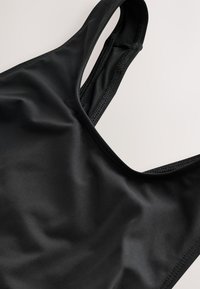 Gros plan d'un soutien-gorge de sport noir montrant un tissu lisse et un design à double bretelle sur un fond clair.