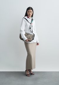 Valge pika varrukaga särk, beežil seotud seelik, mustad rihmik sandaalid. Aksessuaarideks on mustriga salli ja leopardimustriline käekott.