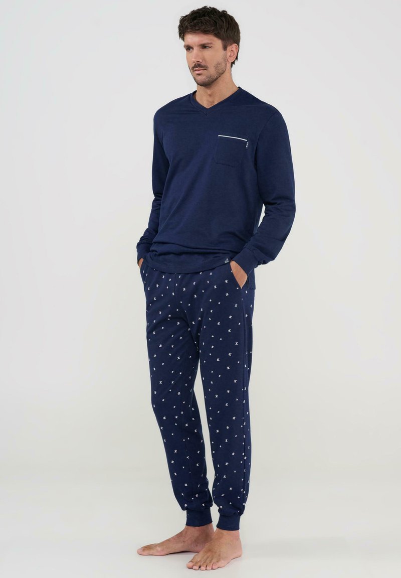 Conjunto de loungewear en navy que incluye una camiseta de manga larga con escote en V y un bolsillo frontal, junto con pantalones jogger estampados que tienen acentos de estrellas blancas.