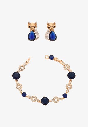 Gouden oorbellen in de vorm van een vos met blauwe druppelstenen en bijpassende gouden armband met blauwe en witte edelsteen schakels.