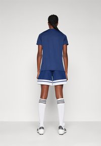 Jersey deportivo de la marina con mangas cortas y franjas en los laterales, combinado con pantalones cortos a juego que tienen un ribete blanco contrastante y calcetas hasta la rodilla.