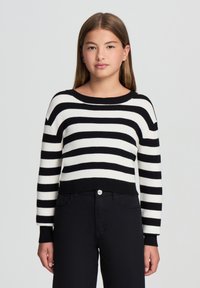 Maglione a righe bianche e nere, texture a coste, scollatura rotonda, vestibilità corta, maniche lunghe, abbinato a pantaloni scuri.