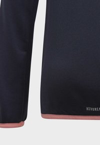 Top deportivo azul marino con tejido texturizado. Presenta un ribete rosa en el dobladillo. Incluye la marca "AEROREADY" en el lateral inferior.