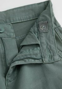 Zielone bawełniane spodnie z suwakiem, zapięciem na guzik oraz teksturowanym paskiem w talii. Posiadają przeszycia dekoracyjne i przednią kieszeń.