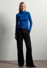 Blue long-sleeve top with mock neck, paired with high-waisted black trousers. Smooth texture, fitted design, and wide-leg shape.