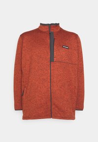 Giacca in pile rossa con colletto alto e design a mezza zip. Presenta una tasca sul petto grigia e tasche laterali, realizzata in materiale a maglia testurizzata.