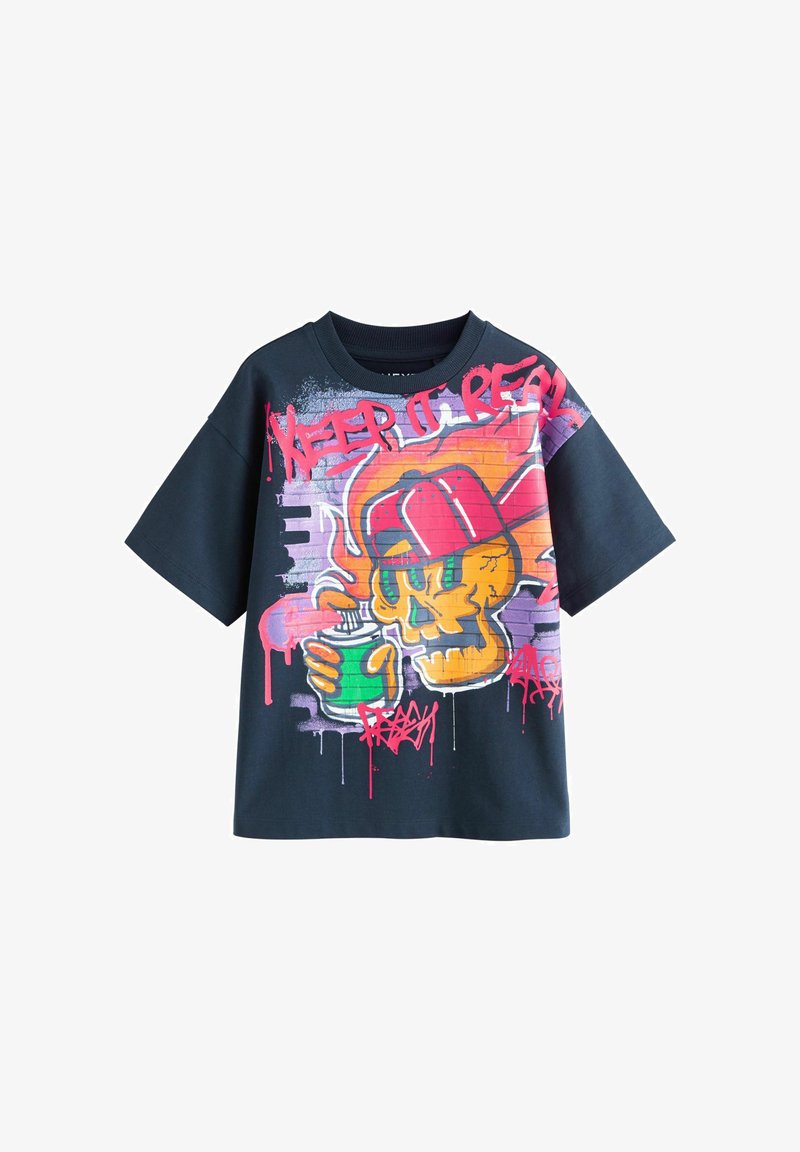 T-shirt noir avec un design style graffiti featuring un crâne jaune portant une casquette rouge, tenant une boisson verte et un texte rouge « KEEP IT REAL ».